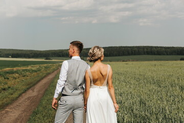 Beautiful happy couple, man and woman are walking in nature together. back view. A young woman in a white dress and a man in trousers and a shirt. Love and Valentine's Day concept.