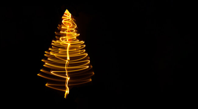 Blurred glowing light painted christmas tree on dark blue background. Copy space. Christmas tree illusion . 