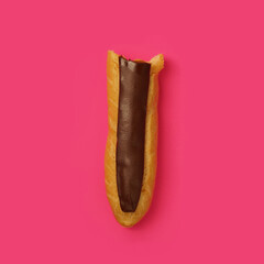 Eclair bitten off with custard and chocolate frosting on a pink background, close-up. Traditional French dessert. homemade baking