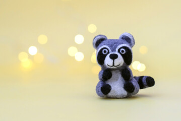 Toy wool raccoon on a yellow background with bokeh