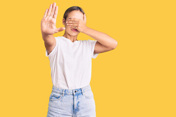 Young beautiful blonde woman wearing casual white tshirt covering eyes with hands and doing stop gesture with sad and fear expression. embarrassed and negative concept.