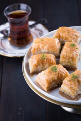 Turkish baklava in white plate with glass of tea in New year setting or decoration on dark wooden background