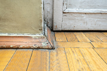 Old scratched pine wood parquet floor in an old house with peeled paint on walls and plinth