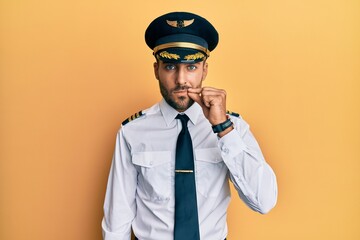 Handsome hispanic man wearing airplane pilot uniform mouth and lips shut as zip with fingers. secret and silent, taboo talking