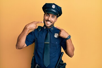 Handsome hispanic man wearing police uniform smiling cheerful showing and pointing with fingers teeth and mouth. dental health concept.