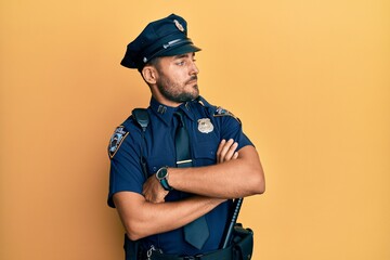 Handsome hispanic man wearing police uniform looking to the side with arms crossed convinced and...