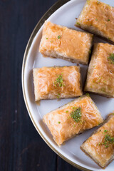 Traditional Turkish baklava in white plate on wooden background, east Mediterranean cuisine, served with black tea