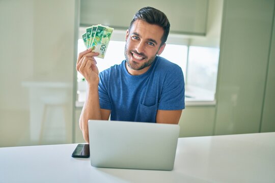 Young handsome man smiling happy holding israeli shekels banknotes at home