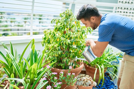 Young handsome man smiling happy caring plants using watering can at terrace