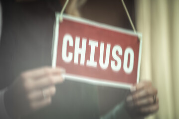 Close up of a females hands holding door sign 'closed'' in Italian