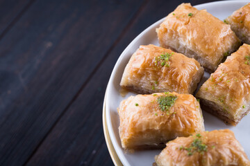 Traditional Turkish baklava in white plate on wooden background, east Mediterranean cuisine, served with black tea