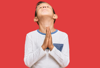 Adorable caucasian kid wearing casual clothes begging and praying with hands together with hope...