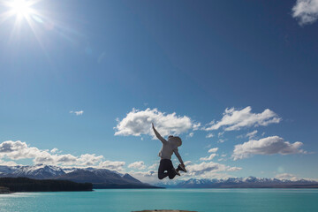 Holiday time! Funny silhouette of young man jumping from the beach by the Tekapo Lake, New Zealand. Concept about lifestyle, travel, nature and people. 