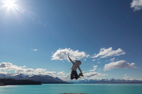 Holiday time! Funny silhouette of young man jumping from the beach by the Tekapo Lake, New Zealand. Concept about lifestyle, travel, nature and people. 