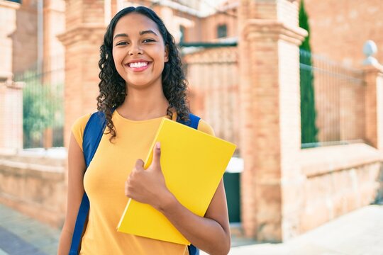 Young african american student girl smiling happy holding book at university campus.