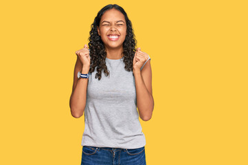 Young african american girl wearing casual clothes excited for success with arms raised and eyes...