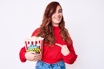 Young beautiful woman holding popcorn smiling happy pointing with hand and finger