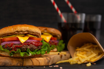 Appetizing burgers on wooden board, glasses with soda and french potato on black background. Fast food concept. Restaurant menu. Cookbook. Classic recipe.