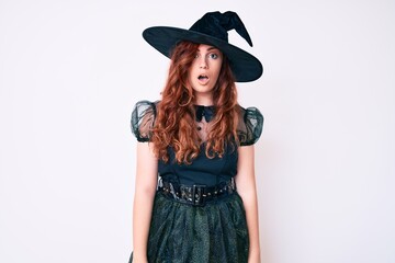 Young beautiful woman wearing witch halloween costume in shock face, looking skeptical and...