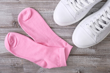 White leather sneakers and pink cotton socks on wooden background, a set for walking and workout