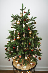 Beautiful little Christmas tree with red and golden balls and gifts in a living room with white walls. Decorated Christmas tree in a modern cozy interior. Concept of New Year and Christmas holidays..