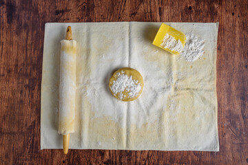 Preparation for baking, ball of sugar cookie dough on a pastry cloth and covered wooden rolling pin on a wood table
