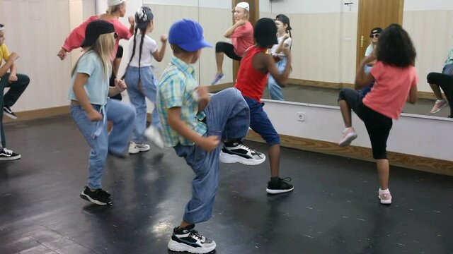 Multiethnic group of children in casual wear training hip hop movements in dance class with female coach