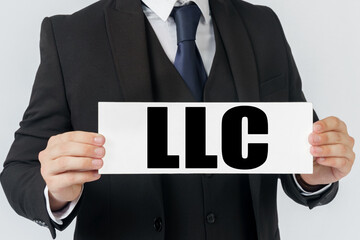 Obraz premium A businessman holds a sign in his hands which says LLC - LIMITED LIABILITY COMPANY