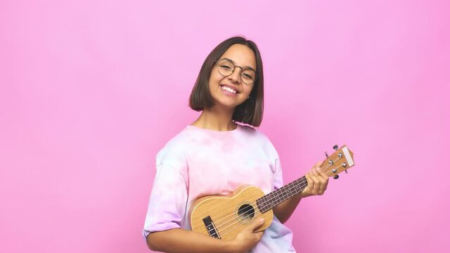 Young latin woman playing ukelele happy, smiling and cheerful