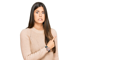 Young brunette woman wearing casual winter sweater pointing aside worried and nervous with...