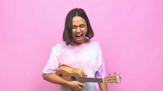 Young latin woman playing ukelele screaming very angry and aggressive