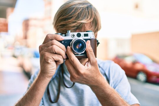 Young irish photographer man using vintage camera at street of city.