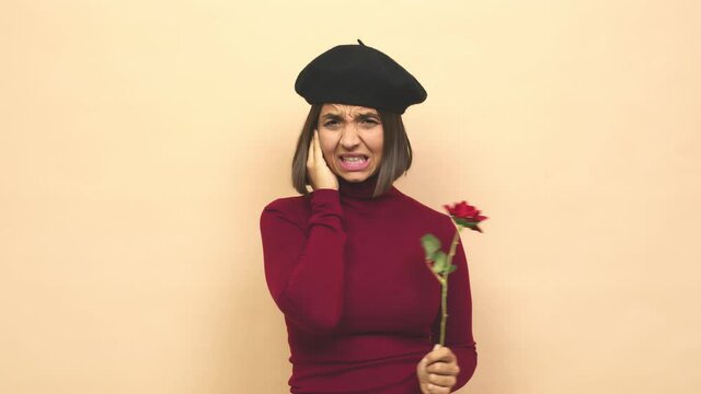 Young latin woman with boina holding rose covering ears with hands