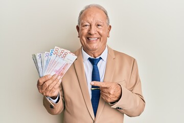 Senior caucasian man holding swedish krona banknotes smiling happy pointing with hand and finger