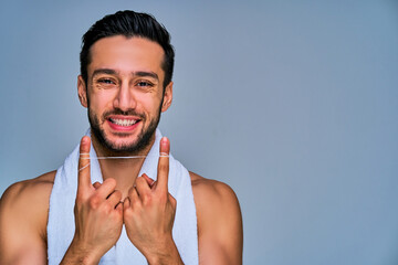 Closeup guy with wide smile with black hair with a beard shows a dental floss on hands. Dental concept