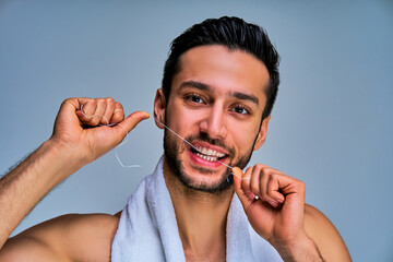 Closeup guy with black hair with a beard brushes teeth with floss stretched on fingers. Dental concept