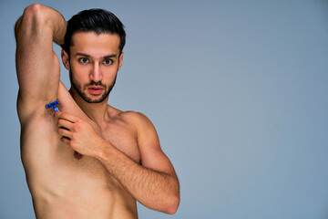 Guy with black hair with a beard with hand up shaving armpit with blue shaver. Beauty concept