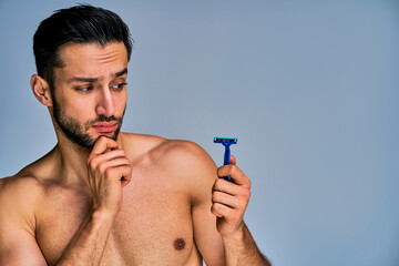 Closeup guy with black hair with a beard looking at the shaver in his hand. Beauty concept