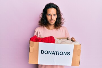 Young handsome man with long hair holding donations box for charity skeptic and nervous, frowning...