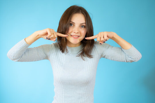 picture of beautiful young woman pointing to teeth over blue background.