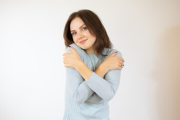 Portrait of a pretty young girl in blue sweater hugging herself. Concept of selfish emotion.