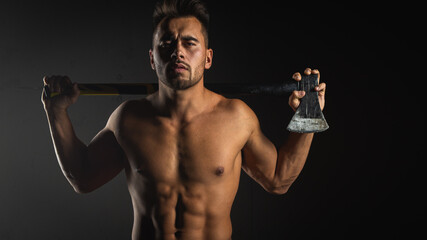 Fototapeta na wymiar young handsome adult, muscular firefighter in uniform holding ax fire equipment in hands, pensive, isolated on dark background. Low key
