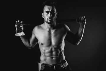 Fototapeta na wymiar young handsome adult, muscular firefighter in uniform holding ax fire equipment in hands, pensive, isolated on dark background. Low key. black and white photo 