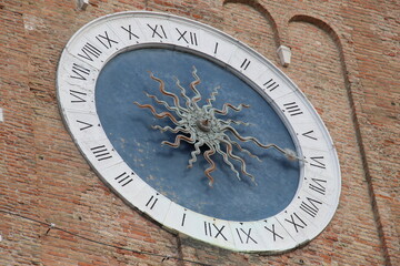 antique church clock on brick wall of church tower sun and sun rays as clock hands on blue clock face, black Roman numerals on white ring