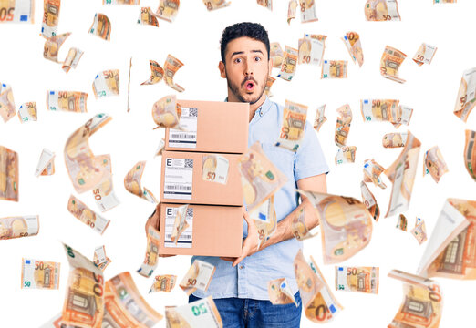 Young hispanic man holding delivery package scared and amazed with open mouth for surprise, disbelief face