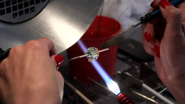 The artist heats the glass with a gas burner. The process of making glass jewelry. Master's hands close-up.