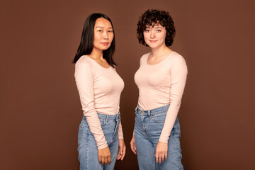 Two young women in white pullovers and blue jeans standing close to one another