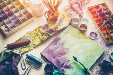 Artistic equipment: canvas and palette knife, paint brushes, multicolored paints in artist studio. Top view.