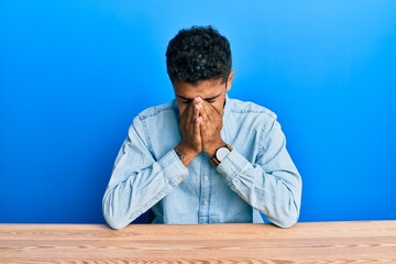 Fototapeta premium Young handsome african american man wearing casual clothes sitting on the table with sad expression covering face with hands while crying. depression concept.
