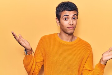 Young african amercian man wearing casual clothes clueless and confused expression with arms and...
